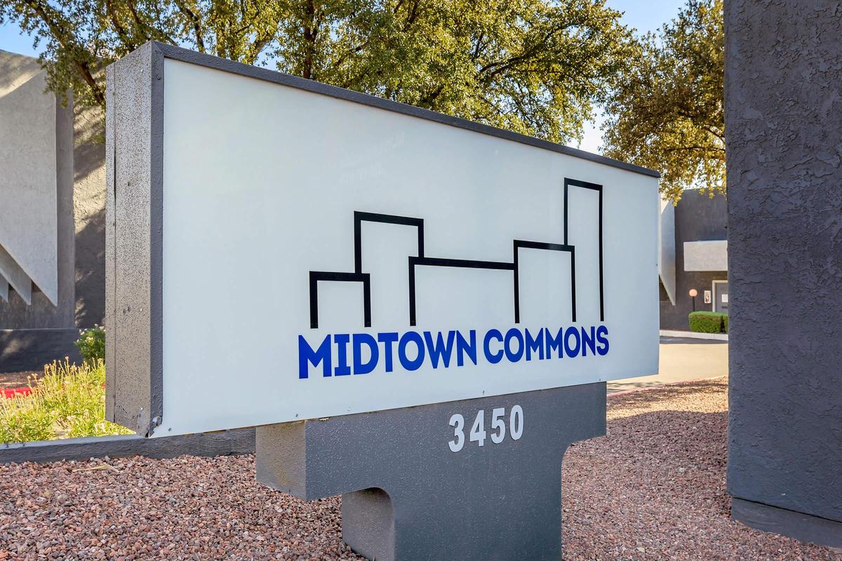 Sign for Midtown Commons, featuring a stylized skyline graphic. The sign is prominently displayed with the address "3450." The background includes greenery and a well-maintained landscape, suggesting a welcoming environment.